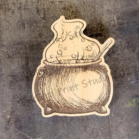 InkBird Print Studio wooden neodymium magnet with laser-etched cauldron, potion bottle, and spoon on dark brown textured wood.